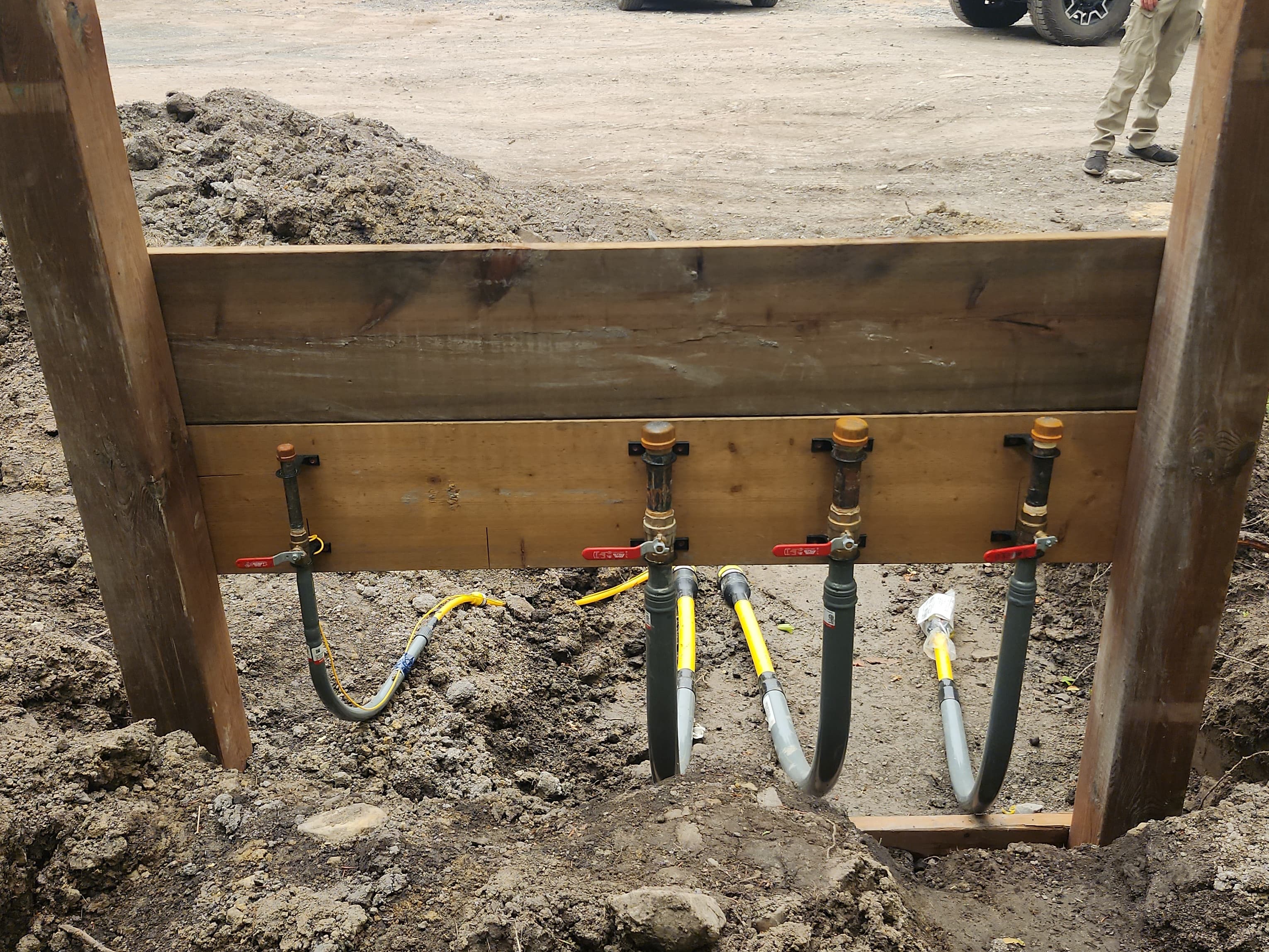 Four gas pipes with red valves mounted on a wooden board at a construction site.