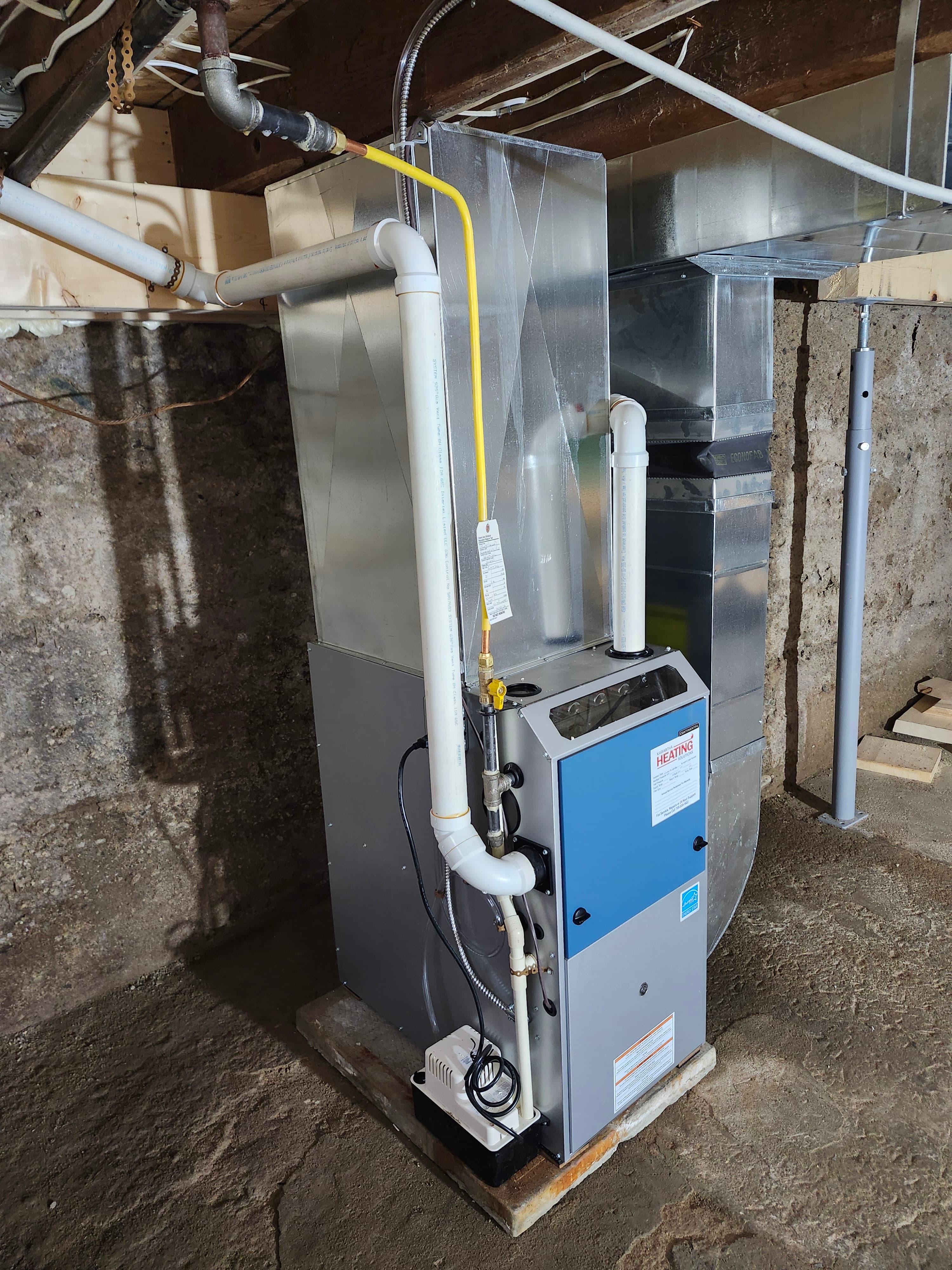 Modern high-efficiency gas furnace with PVC venting and metal ductwork installed in a basement.