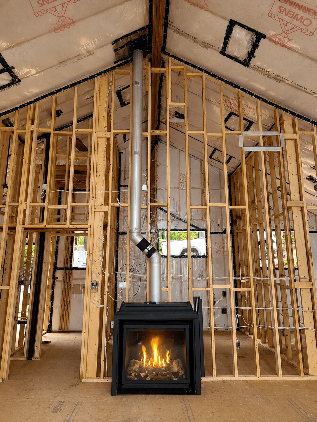 Modern black fireplace with fire burning inside a house under construction with exposed wooden framing.