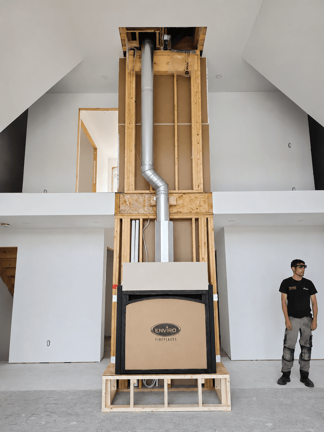 A man stands beside an Enviro fireplace installation with exposed wooden framing and metal flue.
