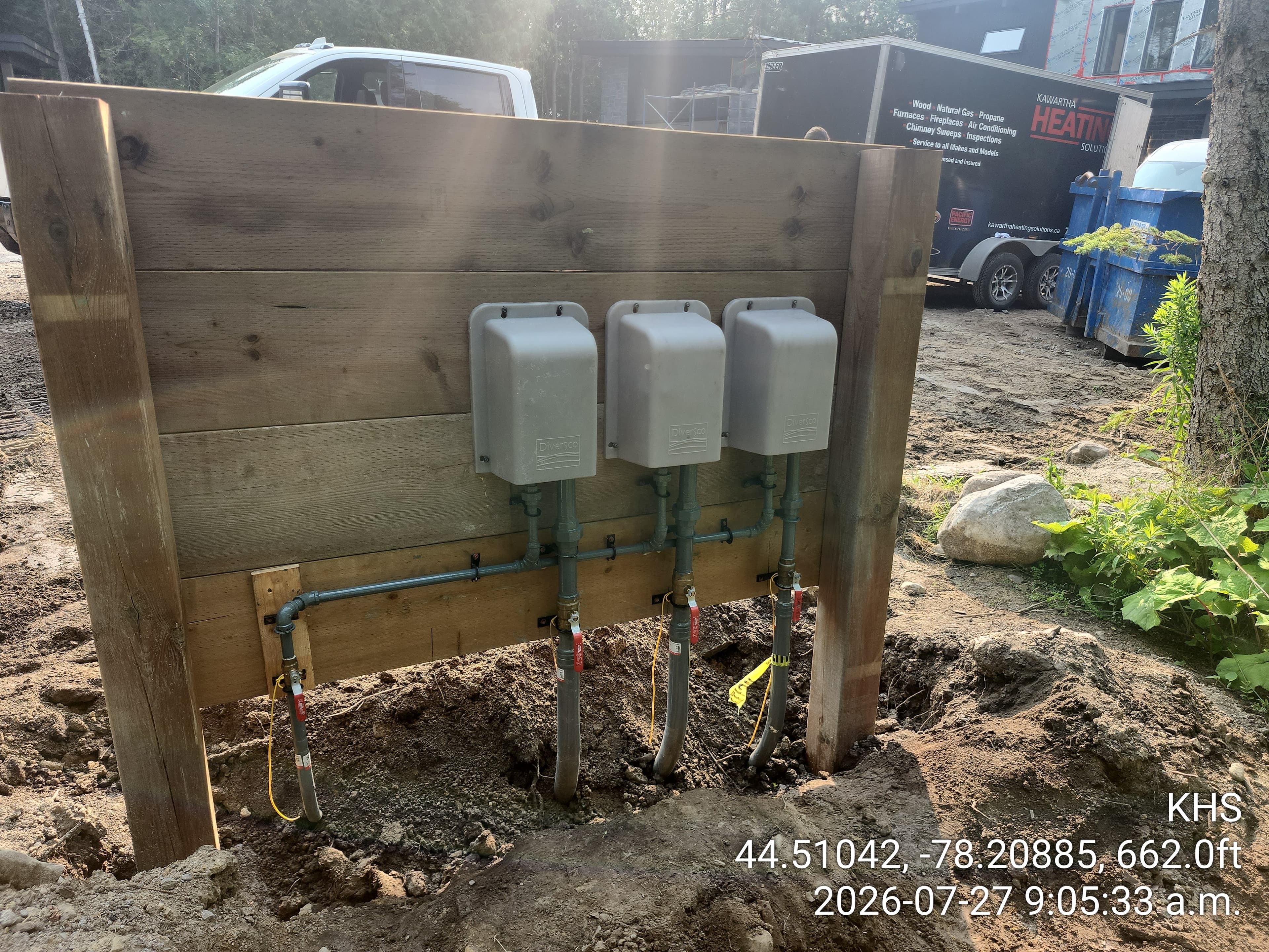 Three gray Diversco utility boxes mounted on a wooden wall with pipes and red valves.