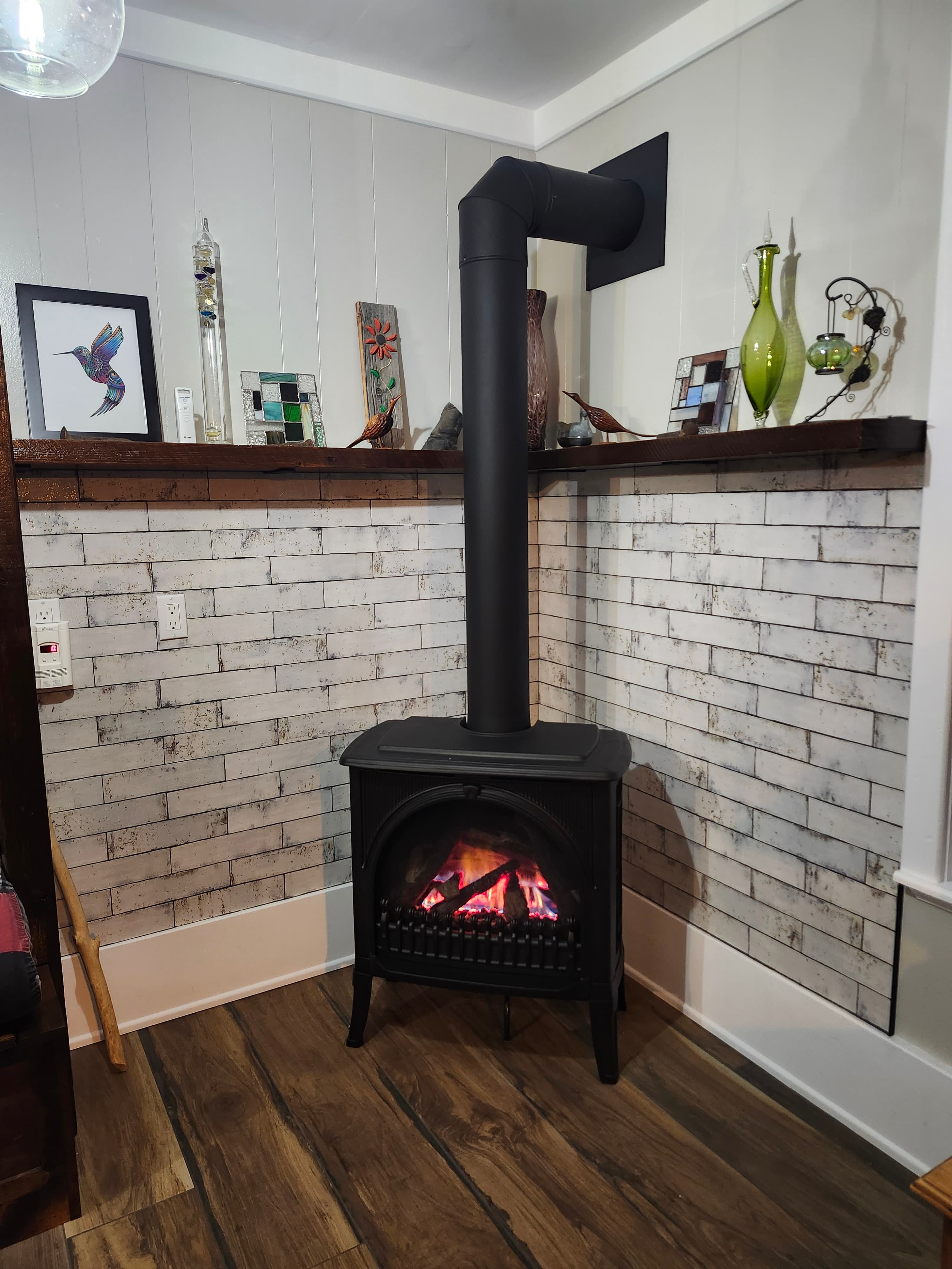 Black wood stove with glowing fire against a distressed white subway tile wall and shelf.