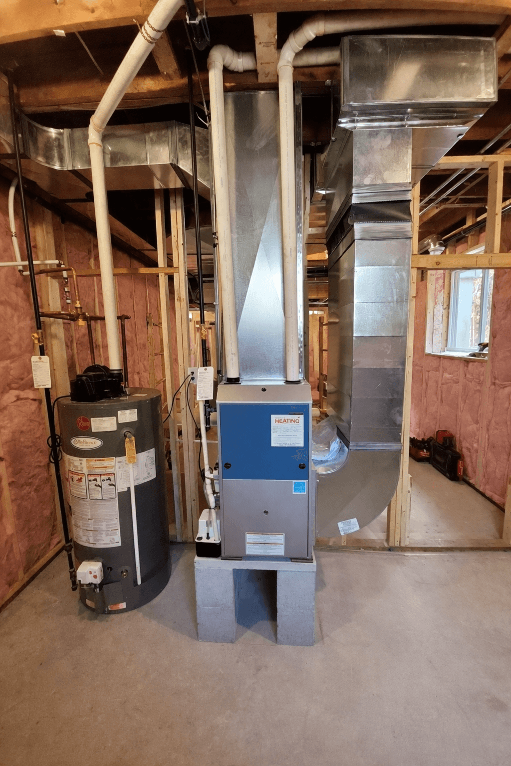 Water heater and furnace with metal ductwork in a basement with exposed pink insulation.