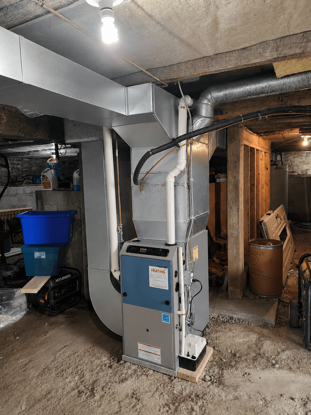 Modern furnace with metal ductwork and white pipes in an unfinished basement with dirt floors.