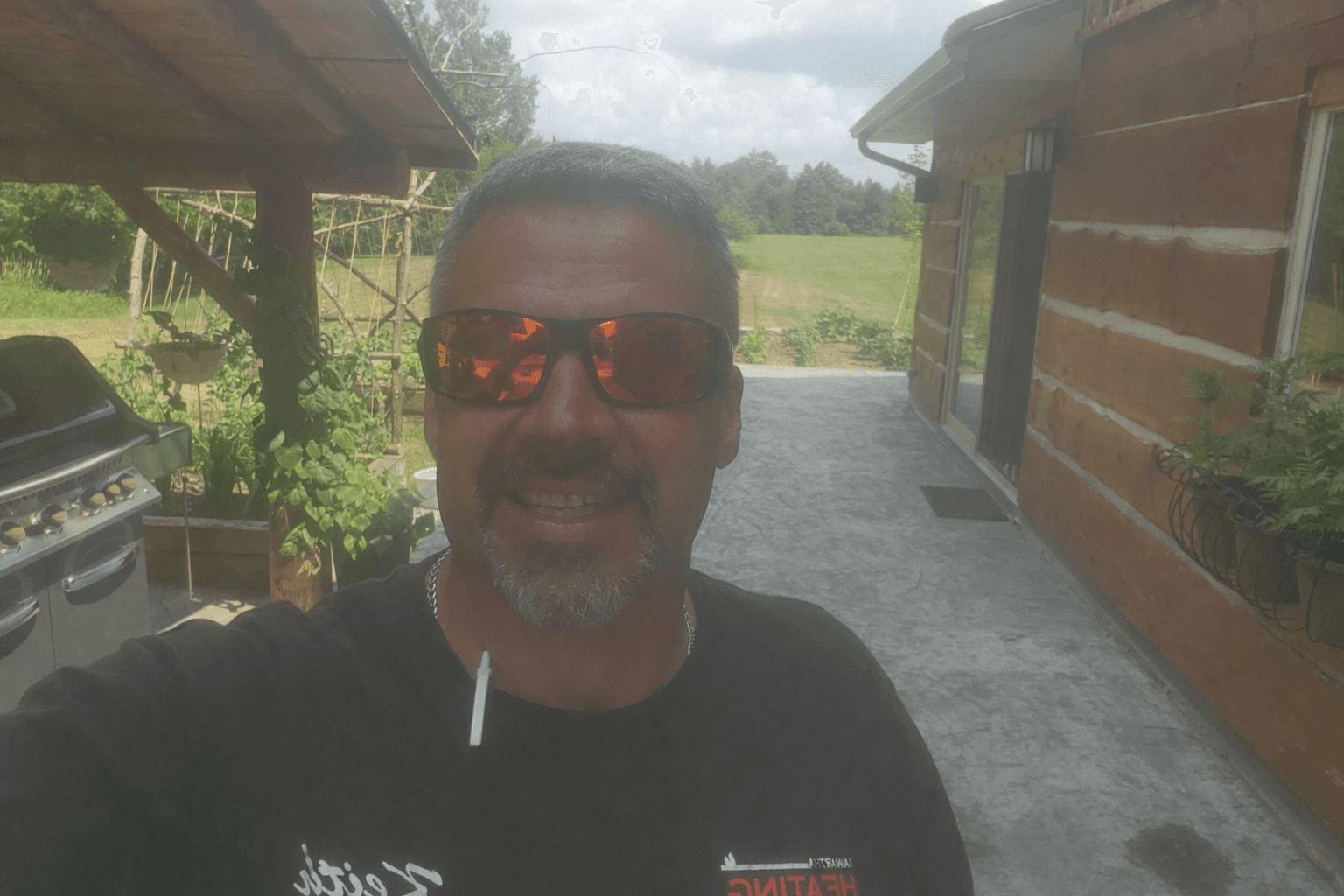 Smiling man with orange sunglasses and goatee standing on a patio outside a log cabin.
