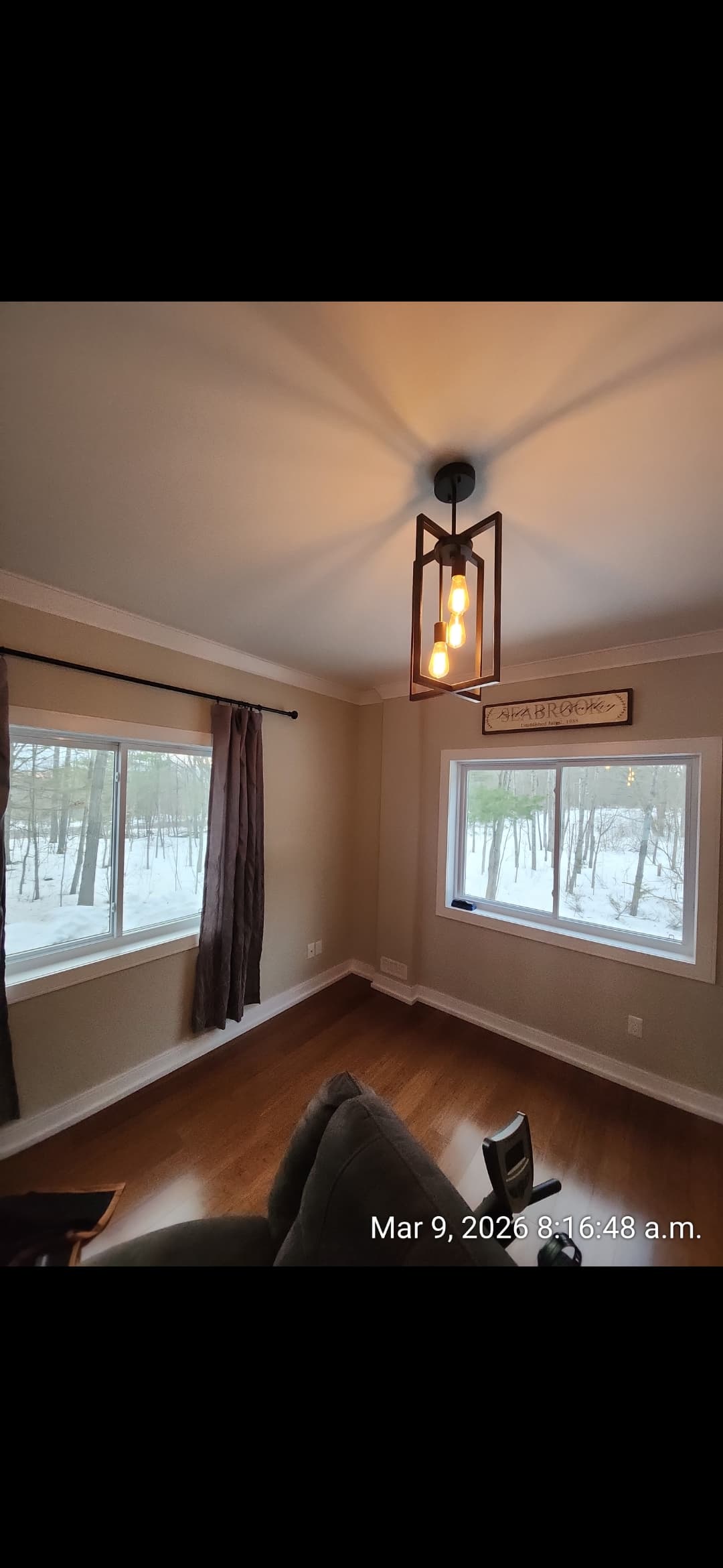 Modern black chandelier in a room with hardwood floors and windows overlooking snowy woods.