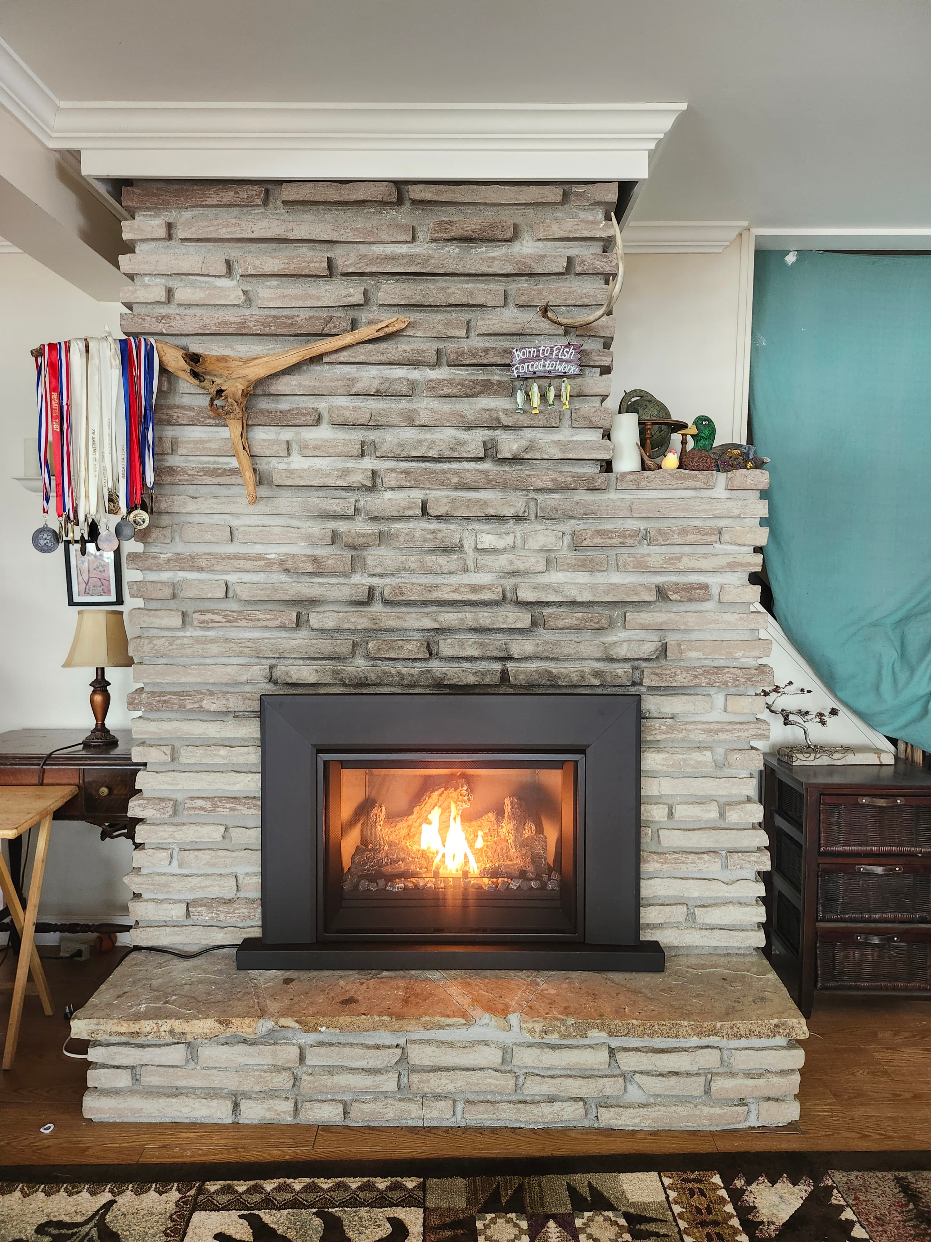 Light brick fireplace with a modern black-framed gas fire burning, decorated with driftwood and medals.