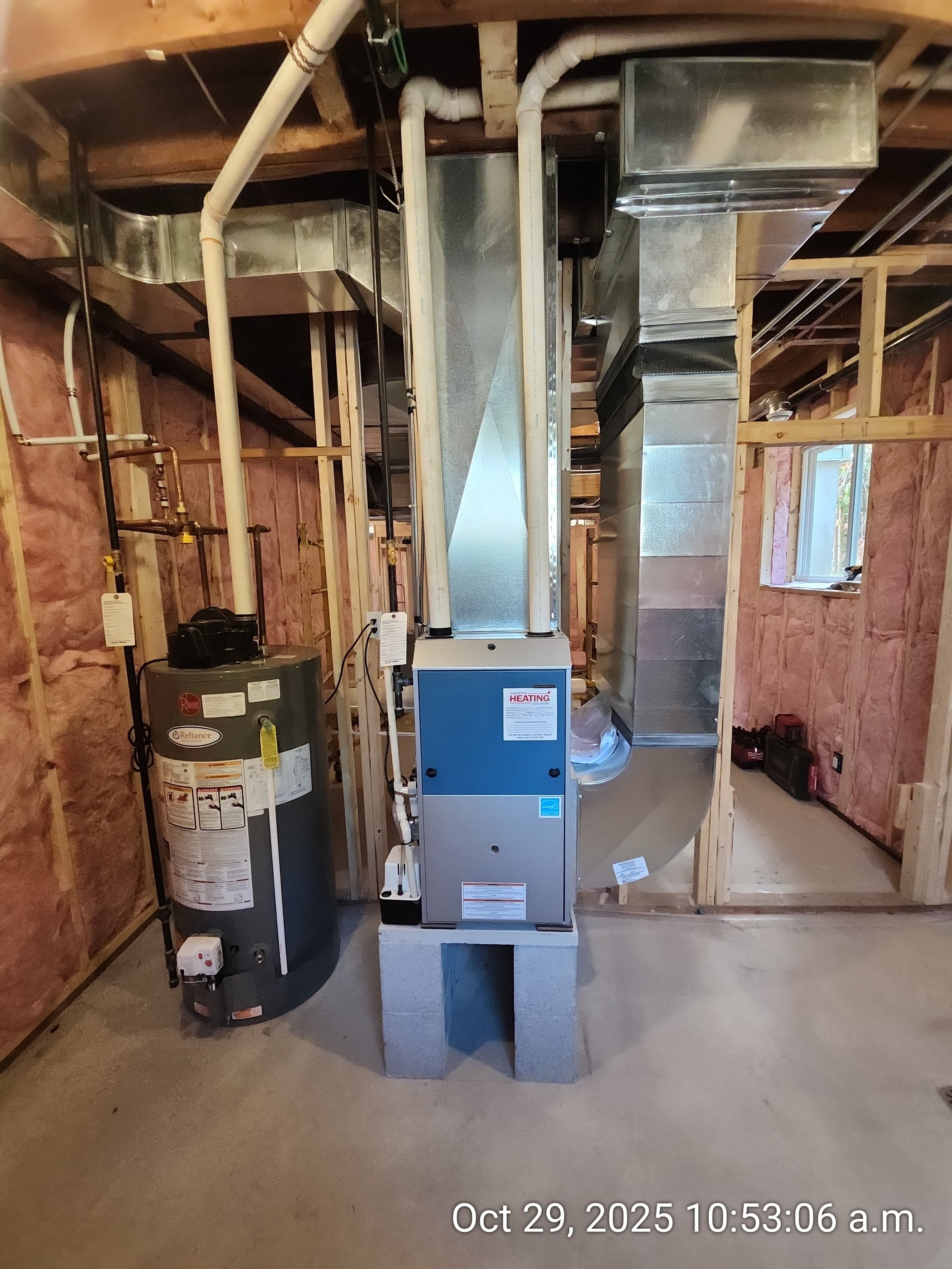 Furnace and water heater with metal ductwork in an unfinished basement with pink wall insulation.