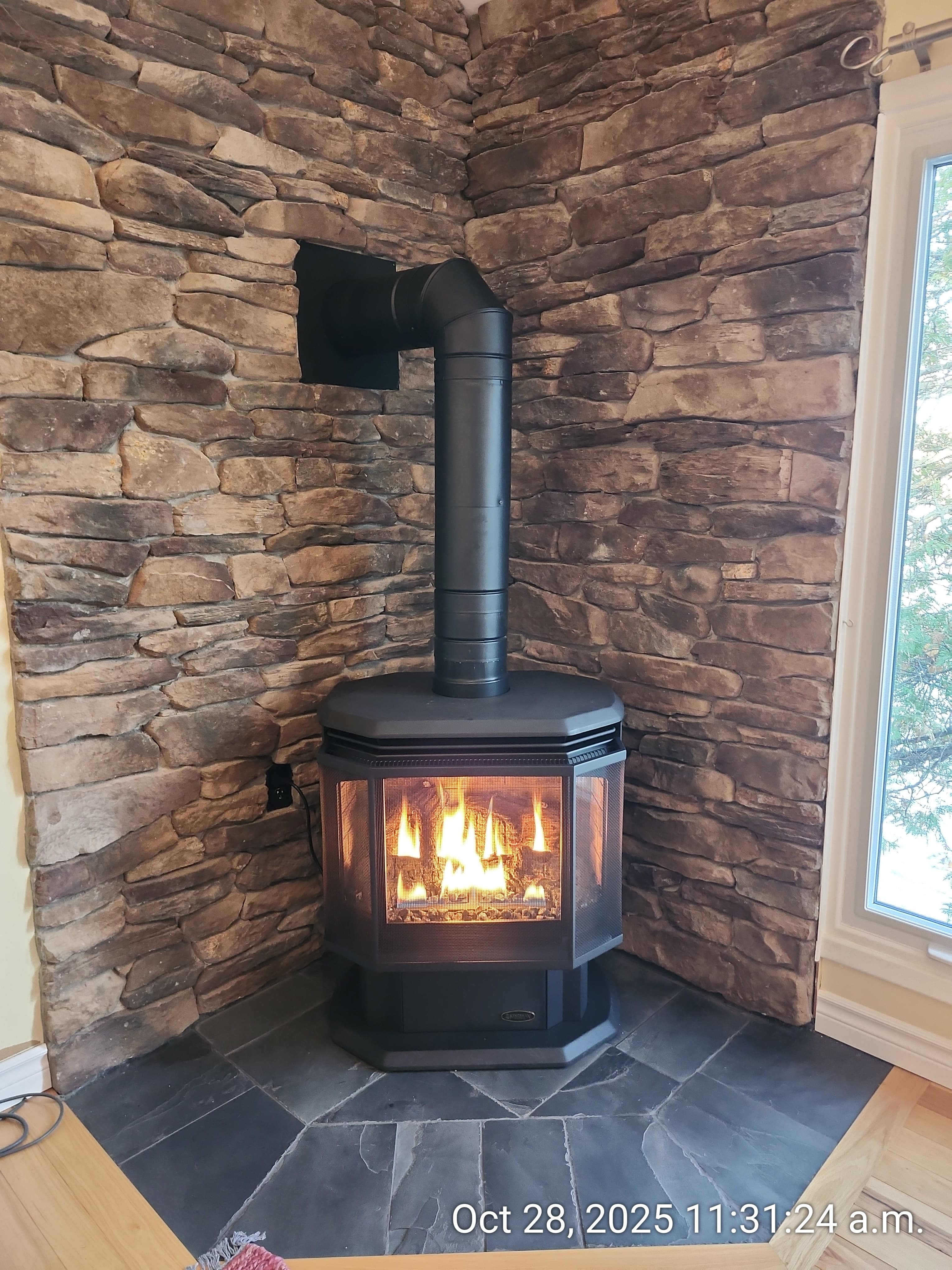 Black gas fireplace with glowing flames against a rustic stone wall in a cozy corner.