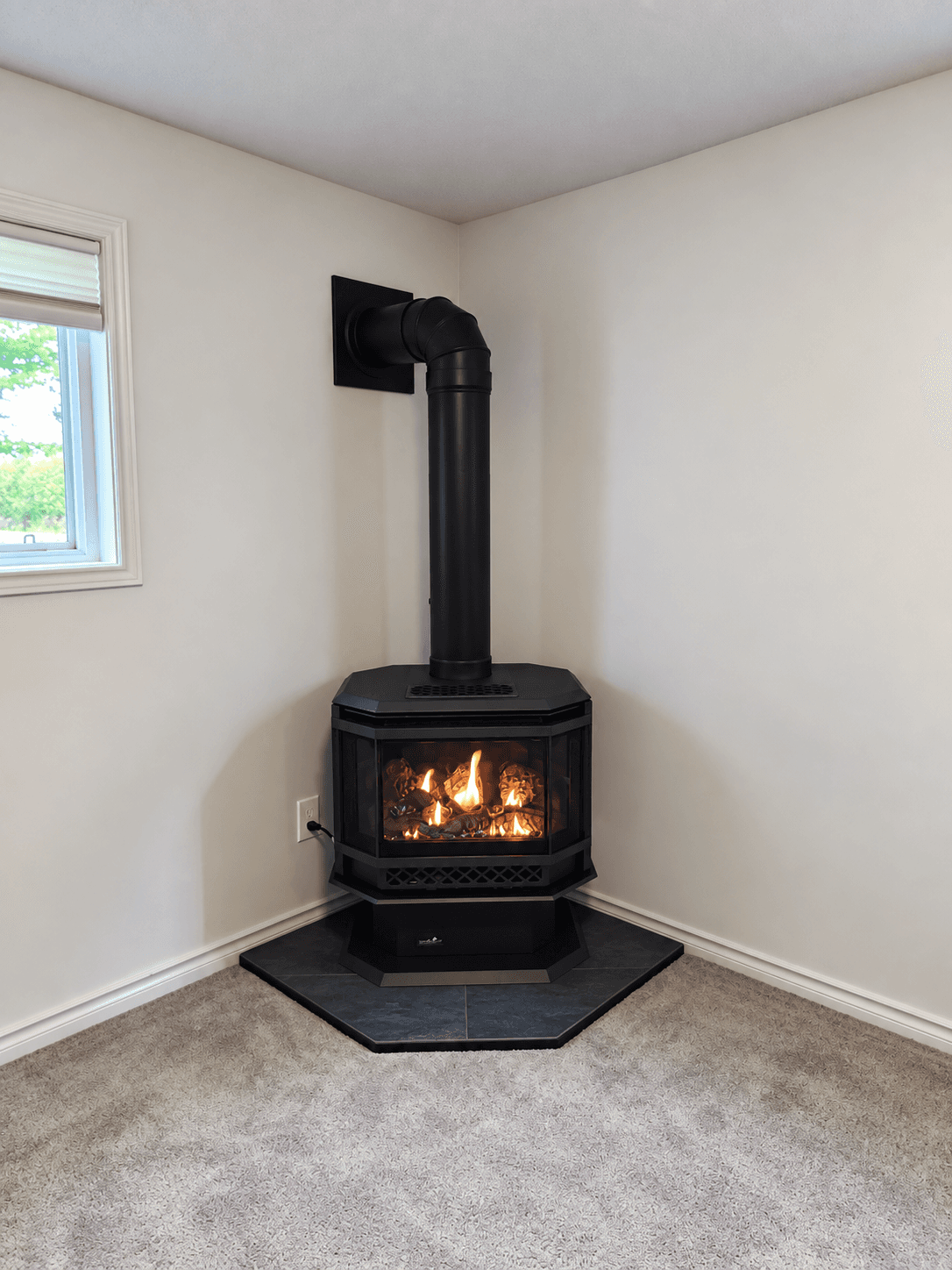 Black gas fireplace with a burning fire, installed in a corner on a stone hearth.