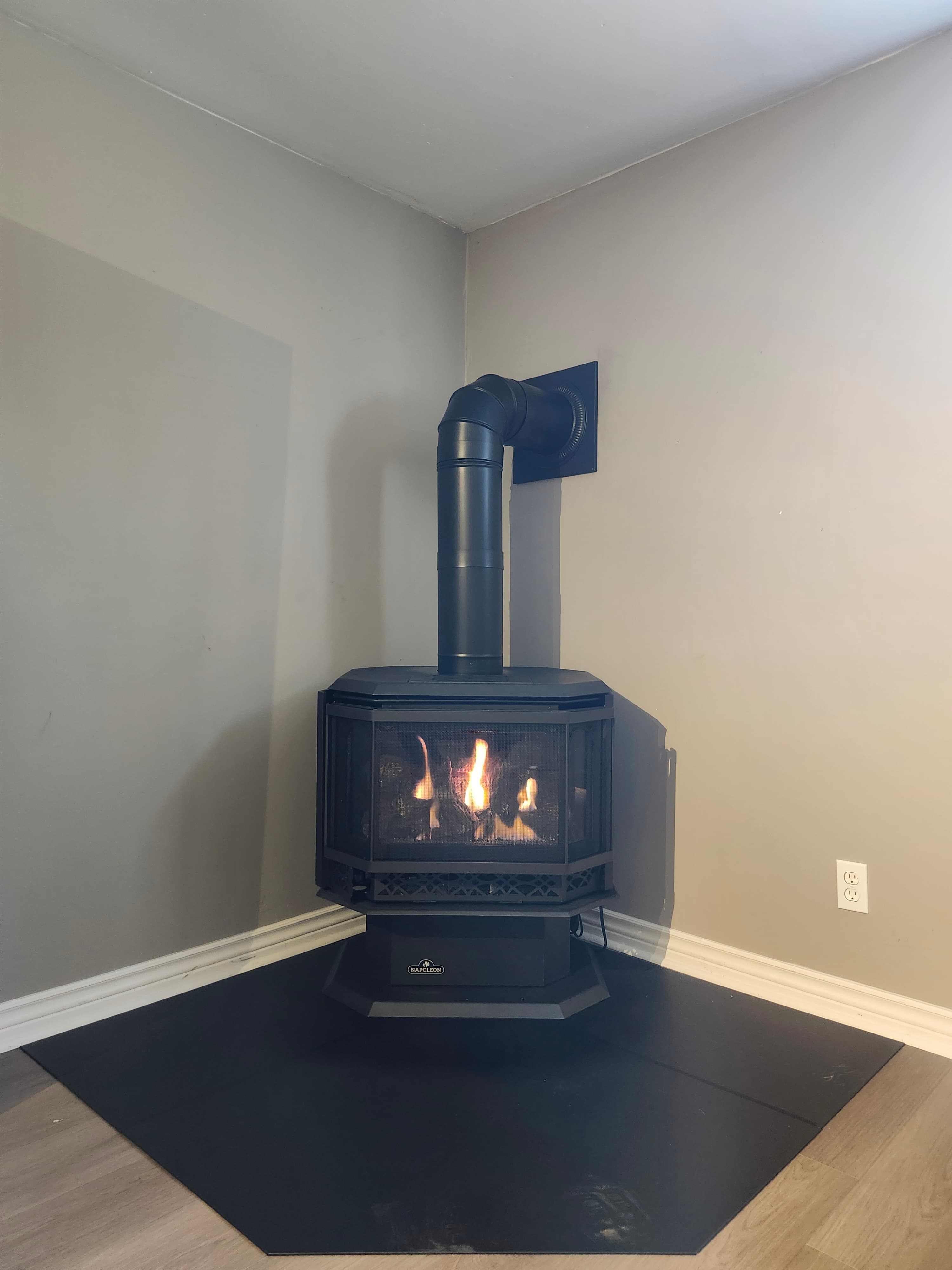 Black Napoleon stove with a burning fire, black exhaust pipe, and black hearth mat.